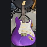 Elektrická kytara s trupem v purpurové barvě s metalickým efektem a bílým perleťovým pickguardem. Nástroj má tři zlaté snímače, tři zlaté ovládací kn…