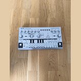 Bílá analogová basová linka syntetizátoru s nápisem TD-3 Computer Controlled Analog Bass Line Synthesizer a logem behringer. Zařízení obsahuje řadu o…