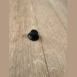 Černý plastový knoflík s kulatým základním tvarováním. Na spodní části je viditelný nápis G. l. 01 a písmeno R. Povrch vykazuje mírné známky opotřebe…