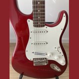 Červená elektrická kytara typu Stratocaster s bílým pickguardem a hnedým hmatníkem. Na spodním snímači je nápis "Dynamic Precision". Kytara má tři bí…