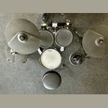 Elektronická bicí souprava v černé barvě s bílým snarem. Na činelech, tamech a snare jsou viditelná loga Roland, přičemž na snare je dále nápis V-Dru…