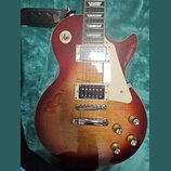 Elektrická kytara typu Les Paul s červeně-žlutým sunburst lakem a viditnou strukturou dřeva. Na hmatníku jsou vidět vložky ve tvaru trapézů a na těle…