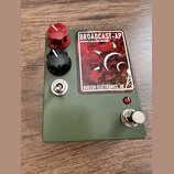 Kytarový pedál v olivově zeleném kovovém pouzdře. Na horní straně je štítek s nápisy BROADCAST-AP, DISCRETE CLASS A PRE-AMPLIFIER a HUDSON ELECTRONIC…
