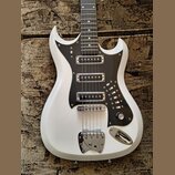 Bílá elektrická kytara s černým pickguardem a chromovaným hardwarem. Na těle jsou tři snímače typu humbucker, jeden ovládací knoflík a chromovaný mos…