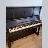 Černé akustické piano s klaviaturou z bílých a černých kláves. Na přední části nad klaviaturou je nápis AKORD v oválném rámečku a v horní části korpu…