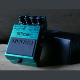 Zelený efekt pedál značky BOSS s modelem Slicer SL-2. Na horní části jsou čtyři ovládací knoflíky a nápisy OUTPUT B, OUTPUT A (MONO), INPUT B, INPUT…