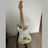 Elektrická kytara s bílým trupem, bílým pickguardem a světle hnědým hnedobělým hmatníkem. Na hlavě je nápis "Fender" a v dolní části hmatníku u 12. p…