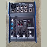 Kompaktní mixážní pult s modrým kovovým rámem a šedým předním panelem. Na horní části jsou nápisy kaifat, ME502 a PREMIUM 5-INPUT 2-BUS MIXER. Zaříze…