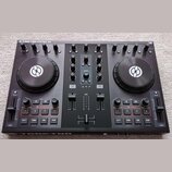 Černý DJ kontrolér s nápisem TRAKTOR KONTROL S2 v levém horním rohu. Zařízení má dva velké jog-kola s bílým logem, zahlreichetočítka a posuvníky. Pov…