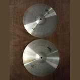 Dva kovové činely v barvě stříbra s koncentrickými drážkami na povrchu. Oba mají v horní části nápis ABX Cymbals a v dolní části označení 14" HIHAT.…