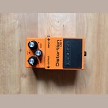 Oranžový efekt pedál s černým spínacím tlačítkem. Na zařízení jsou nápisy Distortion DS-1 a BOSS, dále popisky ovládacích prvků DIST, LEVEL a TONE a…