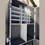 Otevřený transportní case s černým povrchem a hliníkovými hranami. Horní část obsahuje vložku z šedé pěny s mřížkovým členěním pro uložení kabelů neb…