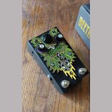 Černý efekt pedál s barevným grafickým motivem v zelené, žluté a fialové barvě. Na povrchu je nápis ZOOMBIE a logo s textem BEETLE JUICE PEDALS. Zaří…