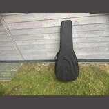 Černý poloměký pouzdro (gig bag) na kytaru. Povrch je z černé textilie s viditelným zipem podél celé délky a menším kapsáři v dolní části. Na pouzdře…