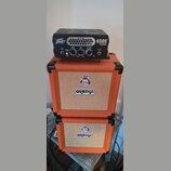 Černý kytarový zesilovač s nápisy Peavey a 6505 PIRANHA™ stojí na dvou oranžových reproduktorových boxech značky ORANGE. Zesilovač má ovládací prvky…