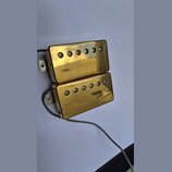 Dva humbuckery s gold povrchem a viditelnými šrouby v polosách. Povrch vykazuje drobné škrábance a známky opotřebení. Z obou snímačů vedou šedé vodič…