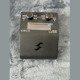 Černý kytarový pedál s nápisy OPUS, AMP SIM a DynIR ENGINE. Horní panel obsahuje dva černé oválné knoflíky a nápisy PERFORM, PRESET, VOLUME, MENU, PA…