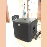 Černý subwoofer s hranatým tvarem a přední kovovou mřížkou. Na mřížce je umístěno bílé logo "EV". Povrch je v matném provedení, horní strana obsahuje…