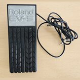 Černý expresní pedál s gumovou protiskluzovou texturou v podobě ševronů. Na horní části je šedý panel s vyraženým nápisem Roland EV-5. K zařízení ved…