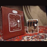 Na fotografii je efekt pedál Electro-Harmonix C9 Organ Machine v bílém rámu s hnědým předním panelem a čtyři černé ovládací knoflíky. Na pedálu jsou…