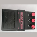 Černý kytarový efekt pedál s nápisy DISTORTION a ADT-1 v červené barvě. Na levé části je vyražen nápis ARIA a dekorativní vlnité linky. Pravá část ob…