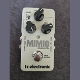 Šedý kytarový efekt s nápisem MIMIC DOUBLER a logem tc electronic. Na horní části jsou tři černé otočné ovladače s popisky TIGHT, ECT a DRY a přepína…