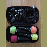 Otevřený černý kufřík s příslušenstvím pro mikrofony. V horní části je smotaný černý kabel, černý mikrofon, USB kabel a tři černé bezdrátové vysílače…