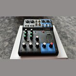 Modrý mixovací pult Yamaha MG06. Na horní části jsou vstupy s nápisy MIC / LINE, L/MONO a R, dále výstupy 5/6 LINE a dva konektory pro sluchátka. Pře…