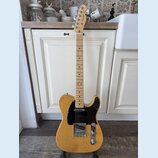 Elektrická kytara s přírodním dřevěným povrchem těla a hmatníkem. Na hlavě je viditelné logo Fender. Kytara má černý pickguard a chromované potenciom…