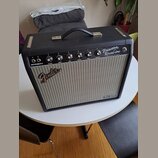 Černý kytarový kombozesilovač s šedou textilní maskou reproduktoru. Na horním ovládacím panelu jsou nápisy Princeton Reverb Amp, FENDER MUSICAL INSTR…