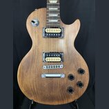 Elektrická kytara s hnědým dřevěným povrchem a dvěma humbuckery. Na přepínači je nápis TREBLE. Kytara má čtyři černé oválné knofíky a stříbrný most s…