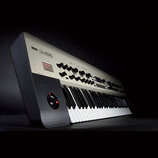 Stříbročerný syntetizátor s klávesnicí a ovládacím panelem. Na horní části je nápis KORG Kronos SYNTHESIZER. Panel obsahuje řadu černých otočných ovl…