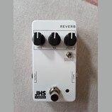 Bílý efekt pedál s nápisem REVERB v horní části. Obsahuje tři černé otočné ovladače s popisky VERB, EQ a DECAY, přepínač PRE-DELAY a v dolní části ná…