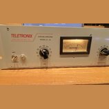 Šedý rackový procesor s nápisy TELETRONIX ENGINEERING CO, LEVELING AMPLIFIER MODEL LA-2A. Zařízení má v pravé části analogový VU metr s nápisem TELET…