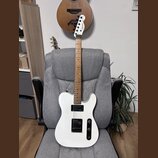 Bílá elektrická kytara s hnědým hmatníkem, opřená o šedé kancelářské křeslo. Na hlavě hmatníku je černý nápis Squier Telecaster. Kytara má jeden sním…