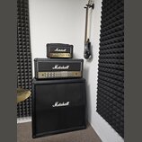 Sada kytarového komba značky Marshall v černé barvě, složená z reproduktorové skříně, zesilovače a menšího modulu. Na všech třech částech je bílý náp…