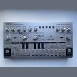 Stříbrný analogový basový syntetizátor s nápisy TD-3 Computer Controlled a Analog Bass Line Synthesizer. Na pravé straně je umístěno logo a značka be…