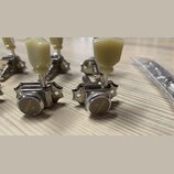 Detailní pohled na čtyři chromované ladicí mechanismy s krémovými plastovými knoflíky. Na kovových krytech je vyryt nápis GOTOH a logo ve tvaru styli…