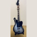 Elektrická basová kytara s offsetovým tvarem korpusu v černo-stříbrném přechodovém lakování. Na hlavě hmatníku je bílý nápis Squier JAGUAR BASS. Nást…