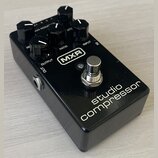 Černý efekt pedál s nápisy MXR a studio compressor. Na horní straně se nachází pět černých otočných ovladačů s bílými značkami a popisky RE, RATIO, A…