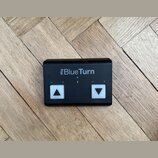 Černý obdélníkový ovladač s nápisem iRig BlueTurn. Zařízení má dvě bílá čtvercová tlačítka s černými šipkami směřujícími nahoru a dolů, nad nimi jsou…