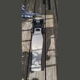 Na dřevěném podkladu leží elektronický pedál basového bubnu v černé a stříbrné barvě. Na spodní části stříbrného šlapadla je umístěn nápis Roland. V…