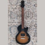 Elektrická kytara s černým korpusem v přechodovém odstínu do hnědého (sunburst) a tmavým hnedým hmatníkem. Na hlavě je bílý nápis Epiphone a vpravo p…