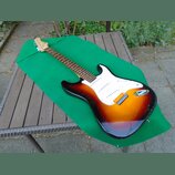 Elektrická kytara s trupem v barevném přechodu od červené přes oranžovou k žluté a bílým pickguardem. Na hlavě hmatníku je nápis Fender Stratocaster.…