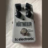 Stříbrný efekt pedál s nápisy RÖTTWEILER DISTORTION, true bypass a tc electronic®. Na horní části jsou čtyři černé oválné ovládací knoflíky a nápisy…