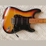 Elektrická kytara s trupem v barevnosti sunburst a černým pickguardem. Na kytare jsou tři snímače typu single-coil, chromovaný most s páčkou a tři ov…