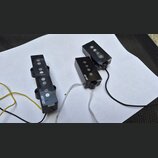 Tři černé elektrické snímače kytary s viditelnými kulatými magnety. Na dvou z nich je bílý nápis MEHTNUI TE. Snímače mají připojené vodiče v barvách…