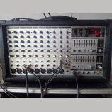 Stříbrošedý napájený mixážní pult v černém kufrovém pouzdře. Na předním panelu jsou nápisy BEHRINGER EUROPOWER, 2 X 250-WATTS STEREO POWERED MIXER WI…