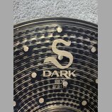 Detailní záběr na povrch činchy v barvě mosazi s černým, nepravidelným broušením. Uprostřed je zlaté logo ve tvaru stylizovaného písmene S a pod ním…