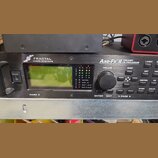 Černý rackový procesor s nápisy FRACTAL AUDIO SYSTEMS a Axe-Fx II PREAMP/ FX PROCESSOR. Zařízení má zelený displej, ovládací knoflík VALUE a řadu tla…